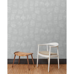 A chair and stool in front of a wall papered in a pattern of white hand-drawn illustrations of New York City landmarks on a gray background.