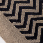 Detail of the Penta Chevron Rug in Jet, a black chevron pattern on a taupe field with a wide solid border. 