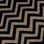 Detail of the Penta Chevron Rug in Jet, a black chevron pattern on a taupe field with a wide solid border. 