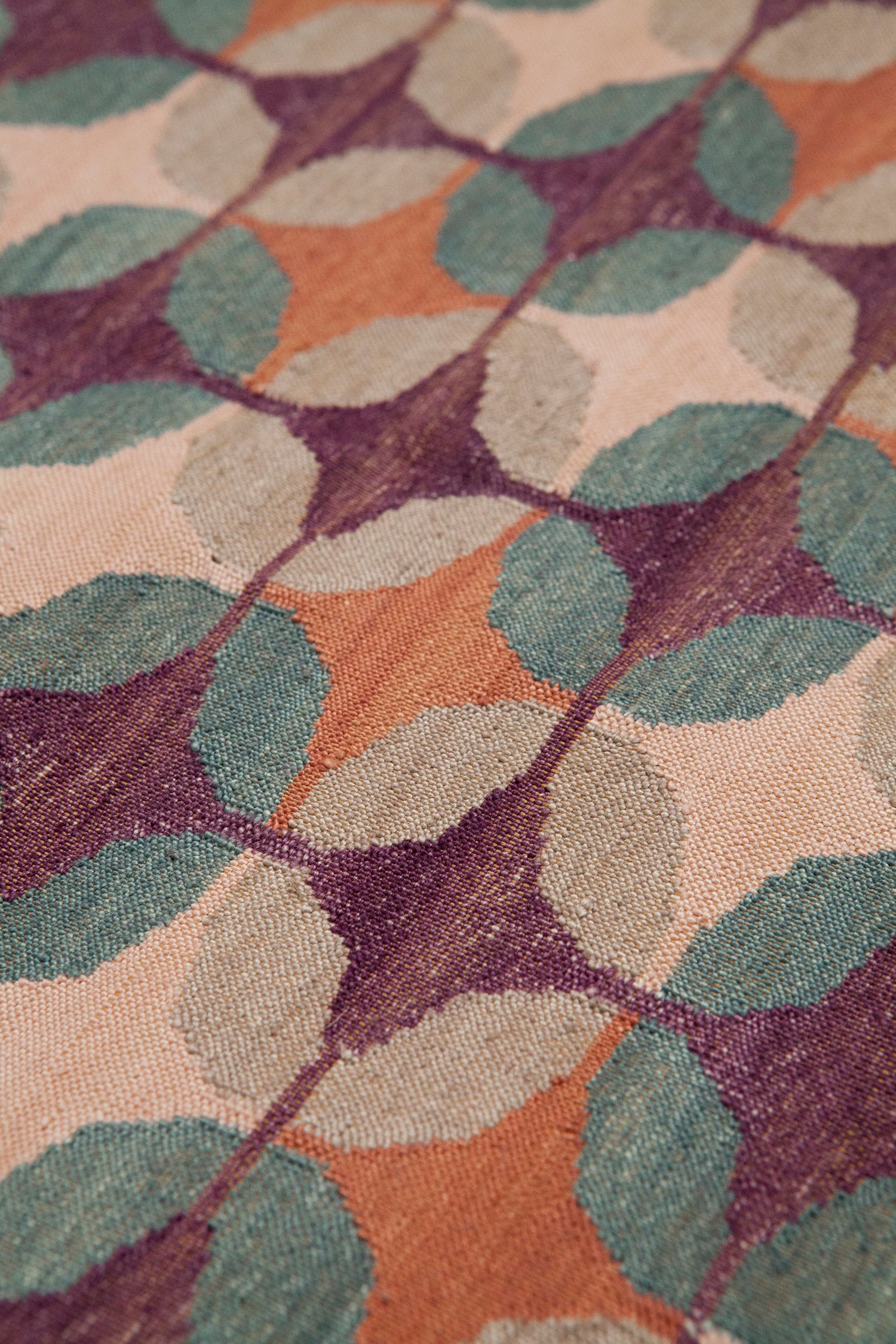 Detail of the Petite Alhambra Rug featuring a pattern of linked circles that create a star like lattice in coral, taupe, turquoise and royal purple. 