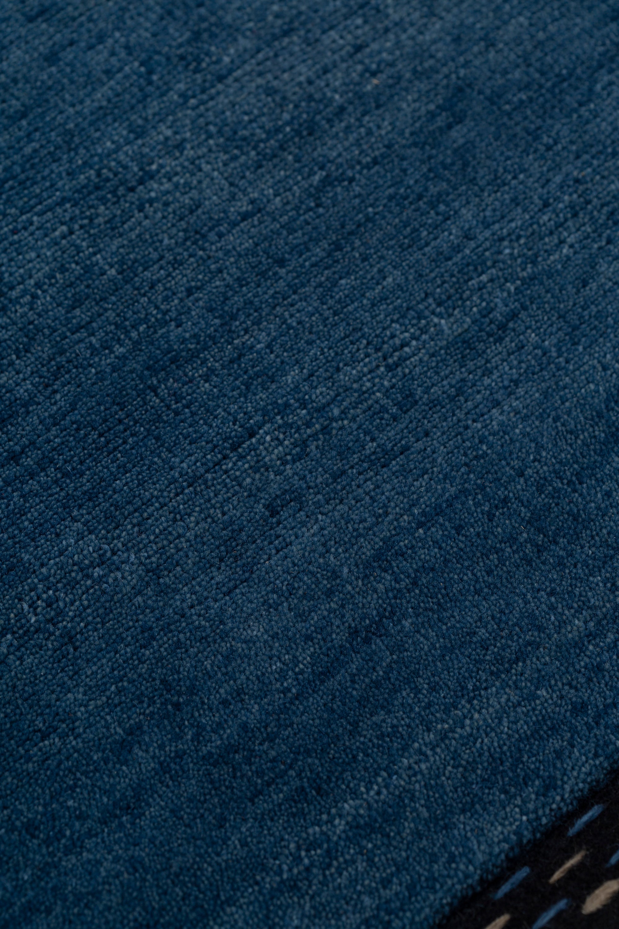 Detail of the Plain Stitched Border Rug in Prussian Blue, a solid indigo rug with a black border with black border with blue and taupe dashes. 