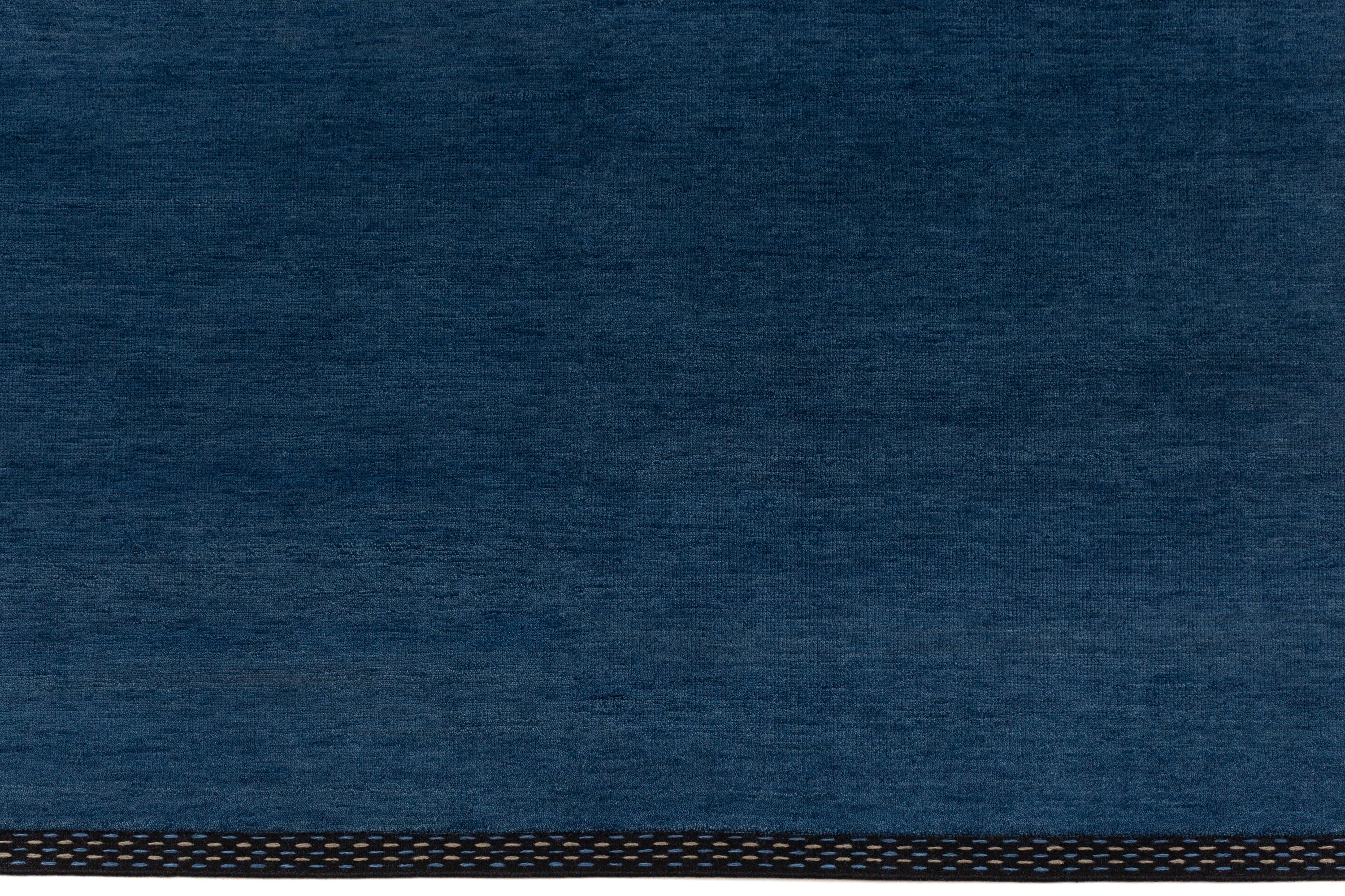 Detail of the Plain Stitched Border Rug in Prussian Blue, a solid indigo rug with a black border with black border with blue and taupe dashes. 