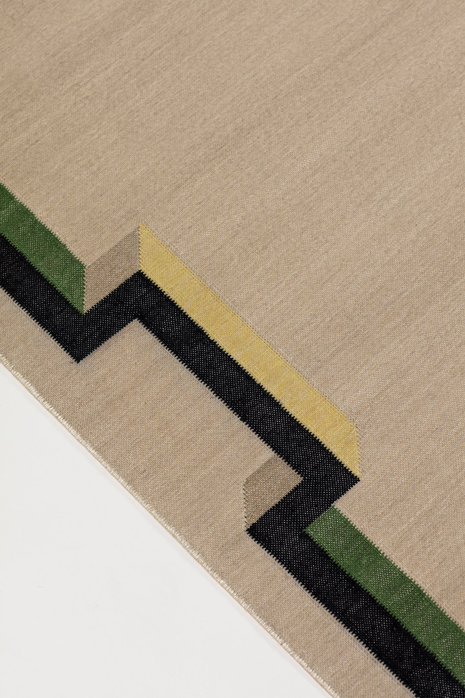 Detail of the Ponti Rug in Salvia, an ivory field with a geometric stair step border in black, with yellow, green and taupe. 