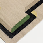 Detail of the Ponti Rug in Salvia, an ivory field with a geometric stair step border in black, with yellow, green and taupe. 