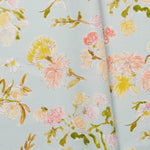Folded linen swatch with a pattern of large-scale line-drawn flowers in gray ink with red, pink and yellow watercolors, on a light blue background.