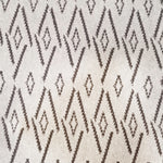Woven broadloom carpet swatch in a repeating irregular diamond pattern in charcoal on a tan field.