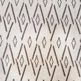 Woven broadloom carpet swatch in a repeating irregular diamond pattern in charcoal on a tan field.