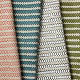 Row of overlapping folded fabrics, each in a honeycomb grid pattern in different pink, blue and green colorways on cream fields.
