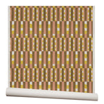 Wallpaper roll with a pattern of vertical stripes of pink, warm olive green and dashes of yellow and white.