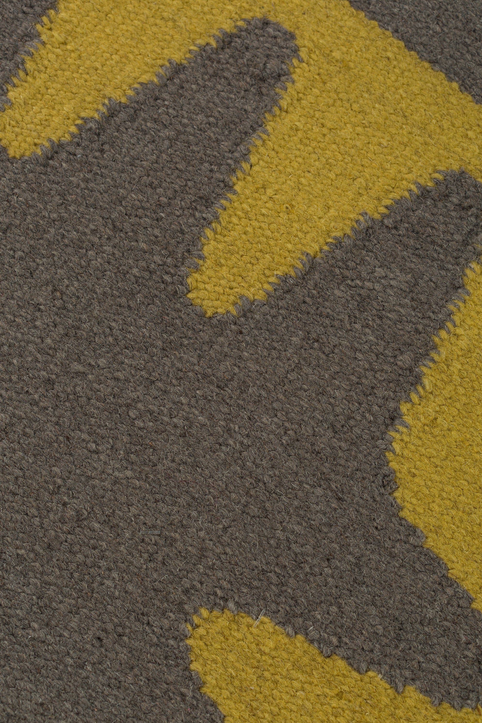 Detail of the Waver Rug in Cardinal Yellow, a dark taupe field with a yellow flame stitch border. 