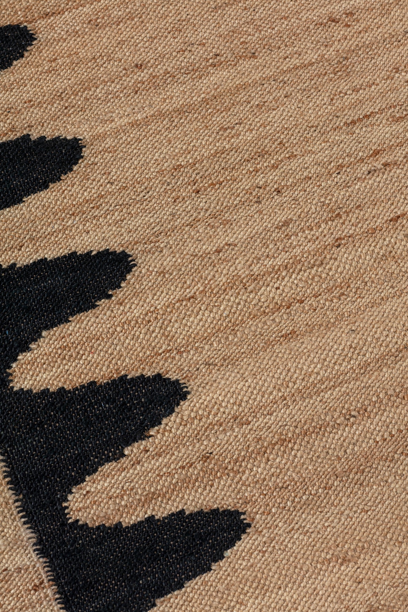 Detail of the Waver Rug in Jet Black, a strated ecru field with a black flame stitch border. 