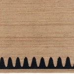 Detail of the Waver Rug in Jet Black, a strated ecru field with a black flame stitch border. 