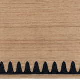 Detail of the Waver Rug in Jet Black, a strated ecru field with a black flame stitch border. 