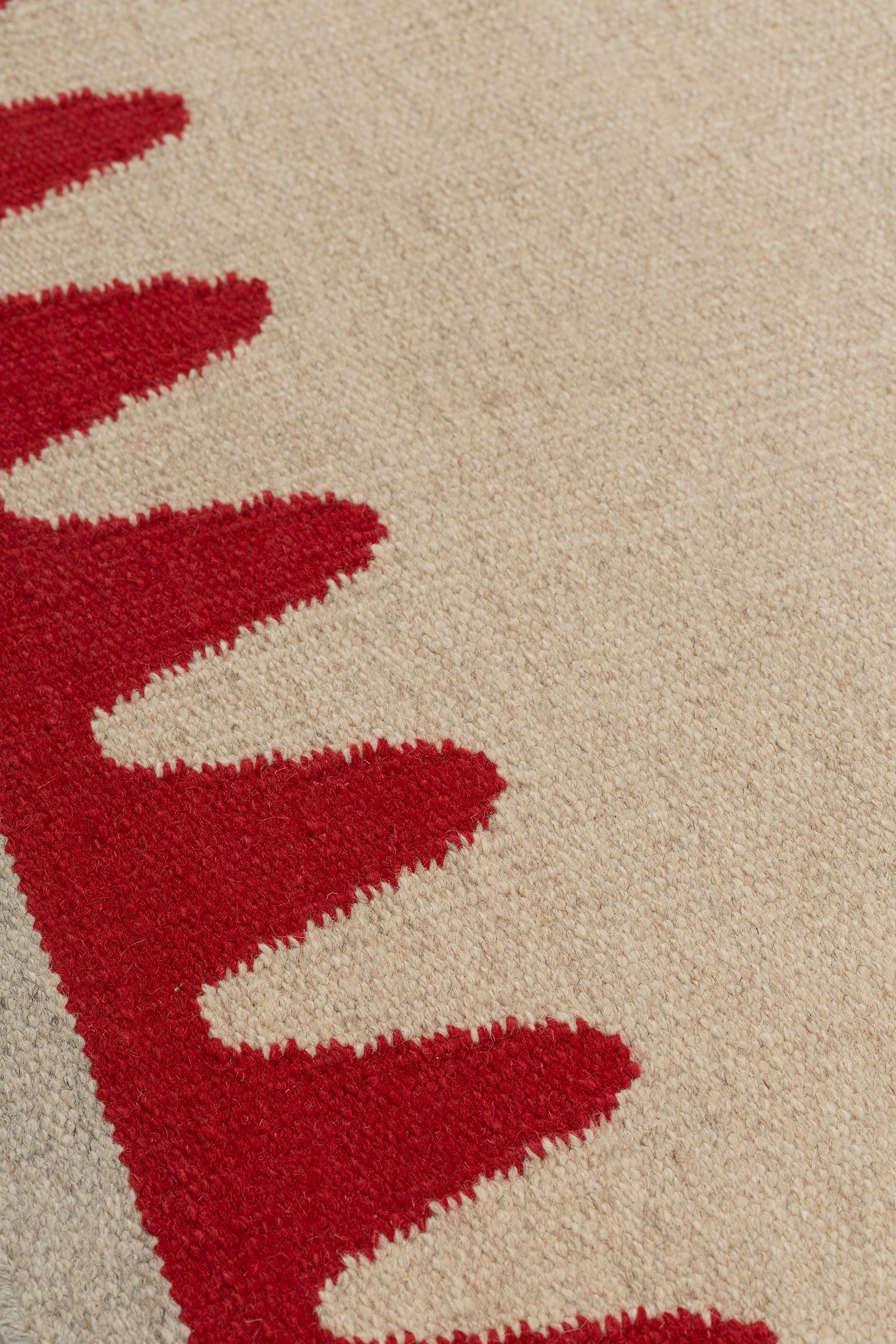 Detail of the Waver Rug in Pillbox Red, a solid Ivory field with a red flame stitch border. 