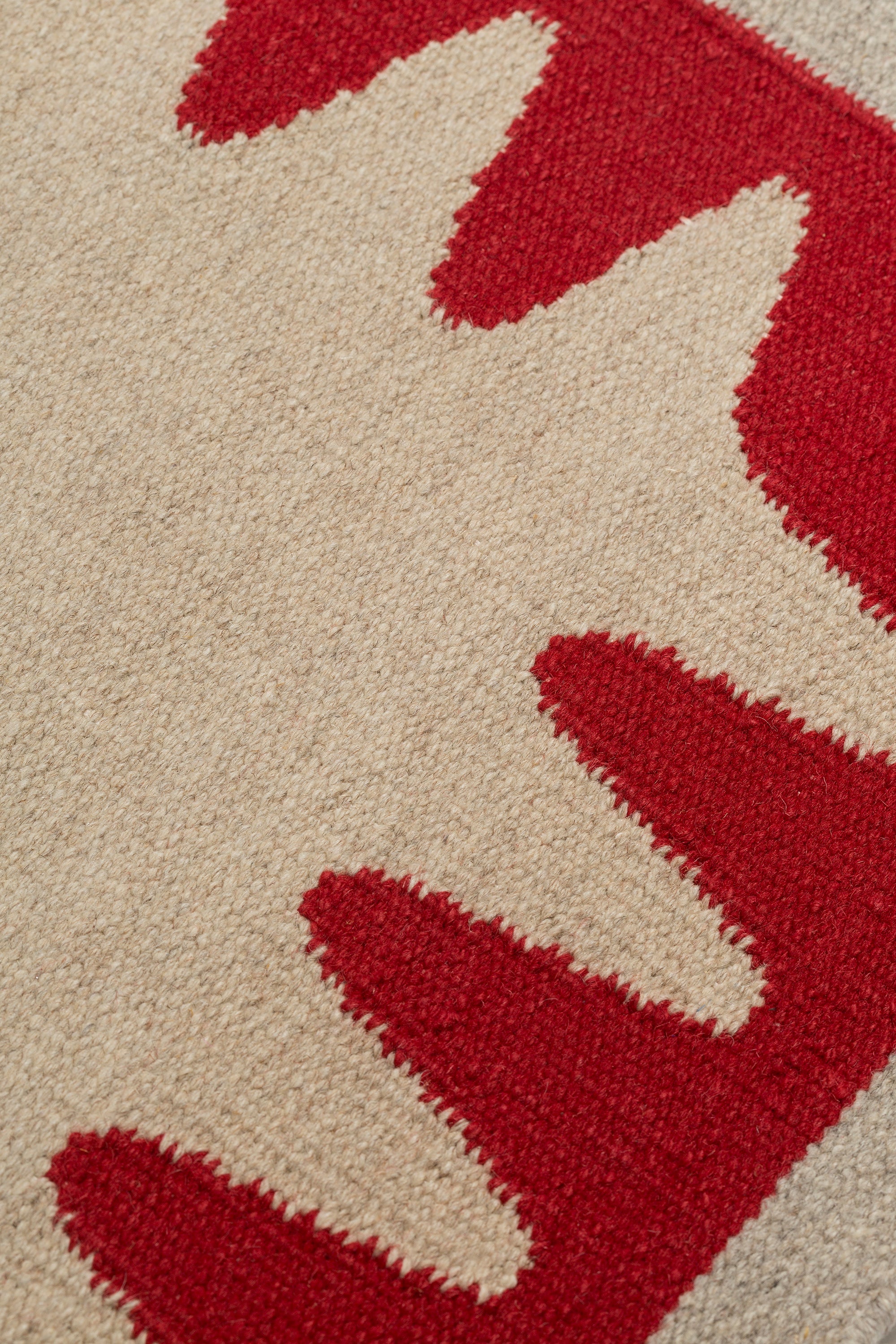 Detail of the Waver Rug in Pillbox Red, a solid Ivory field with a red flame stitch border. 