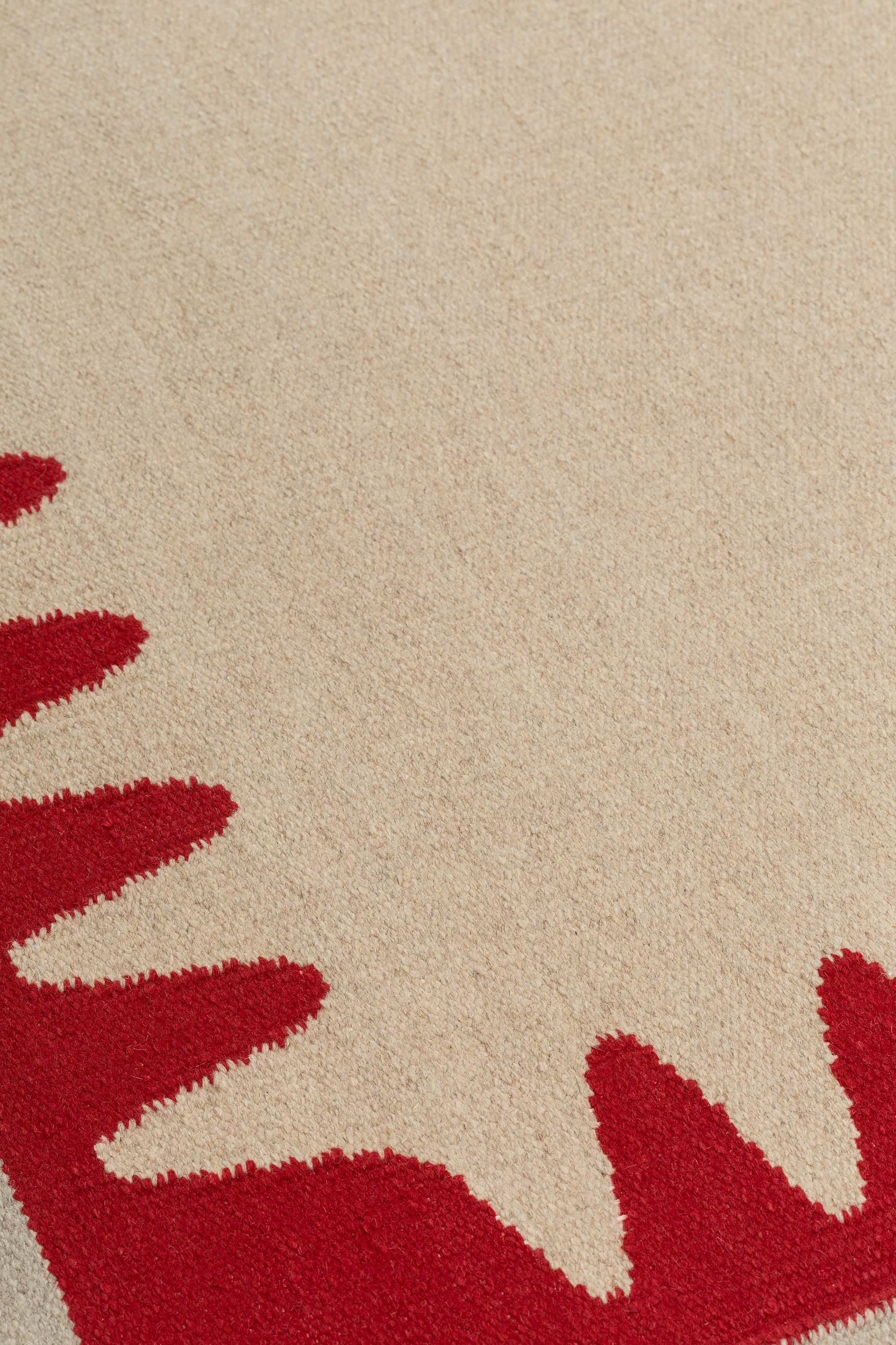 Detail of the Waver Rug in Pillbox Red, a solid Ivory field with a red flame stitch border. 