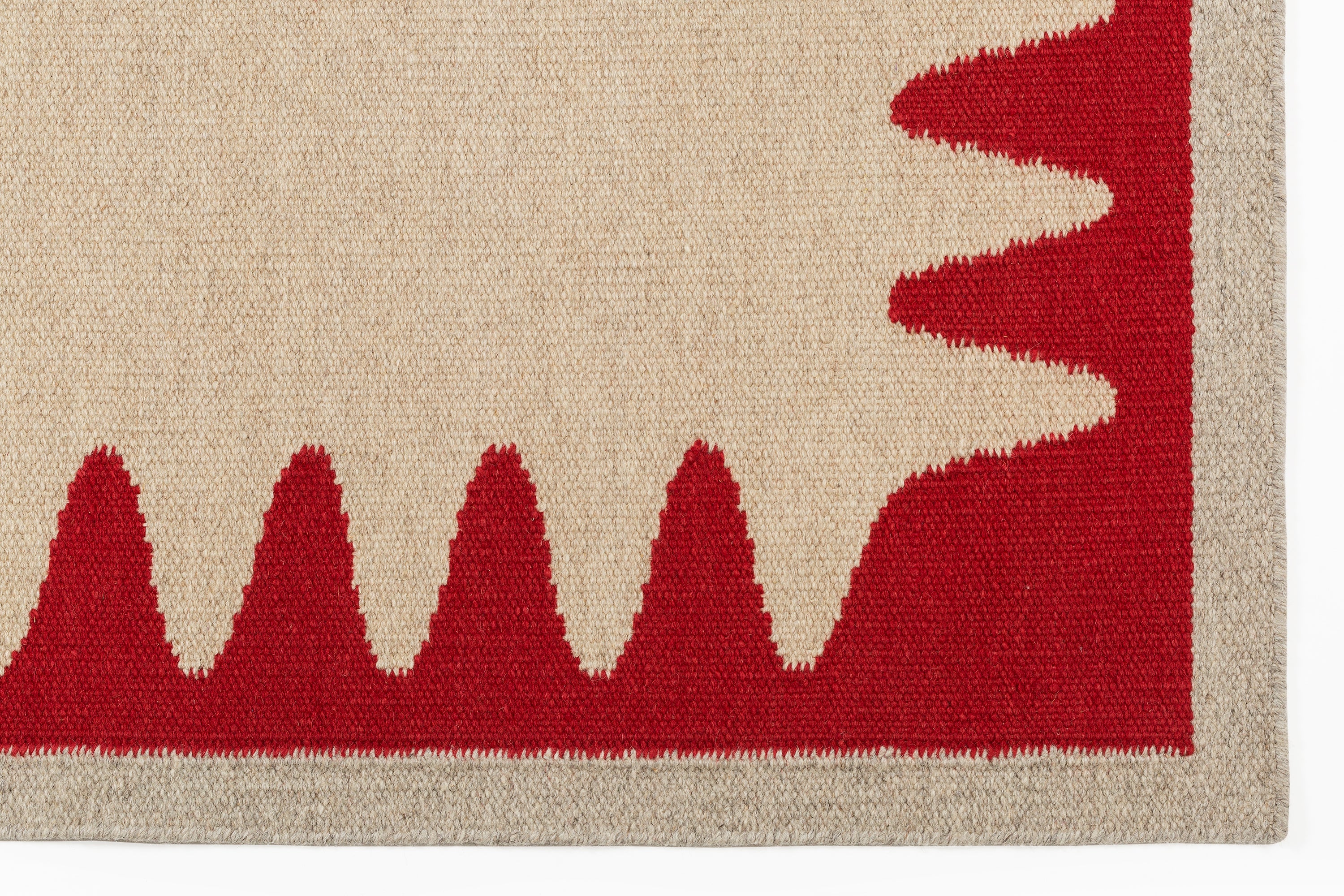 Detail of the Waver Rug in Pillbox Red, a solid Ivory field with a red flame stitch border. 