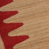 Detail of the Waver Rug in Safflower Red, a strated ecru field with a red flame stitch border. 