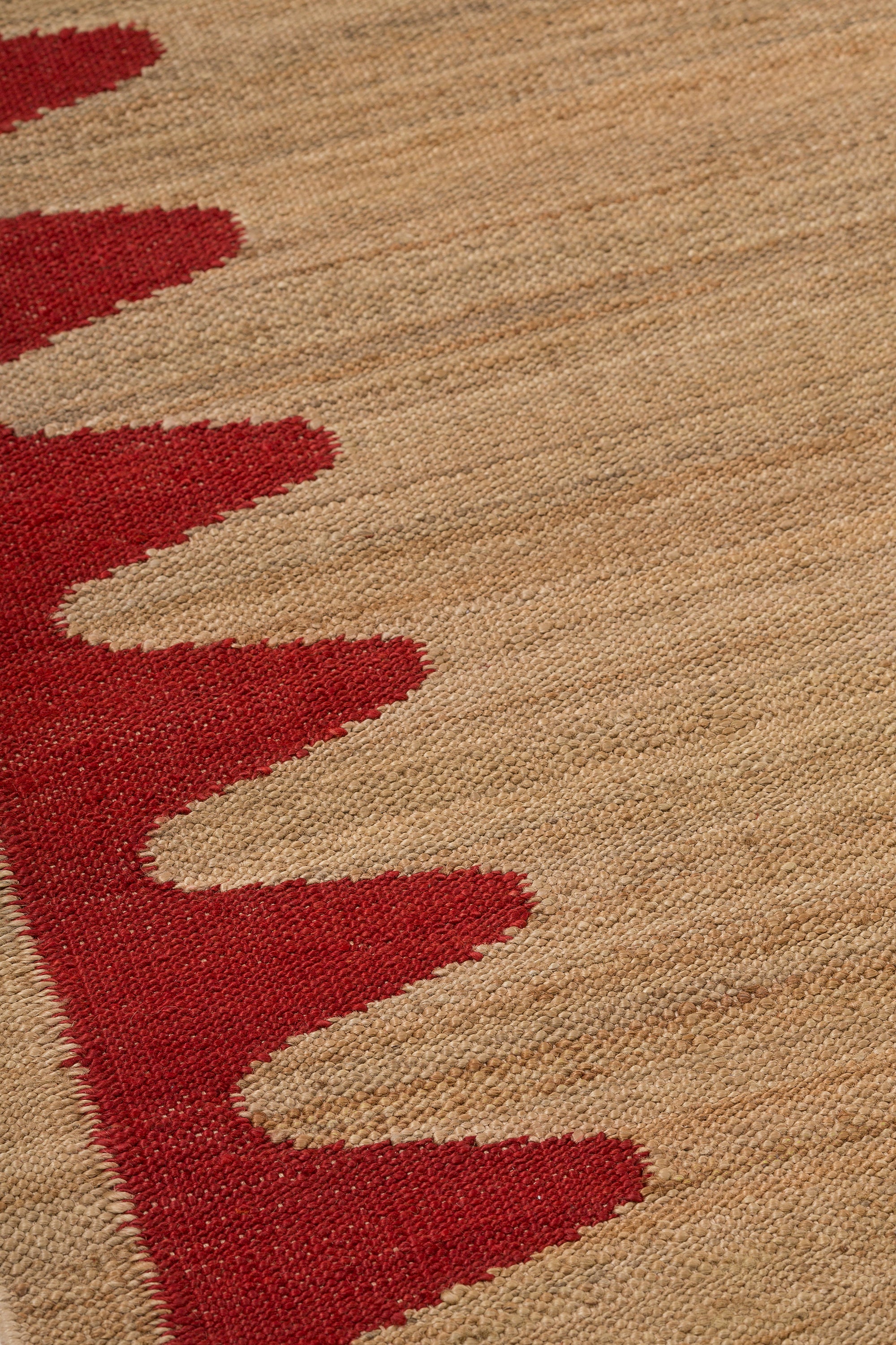 Detail of the Waver Rug in Safflower Red, a strated ecru field with a red flame stitch border. 