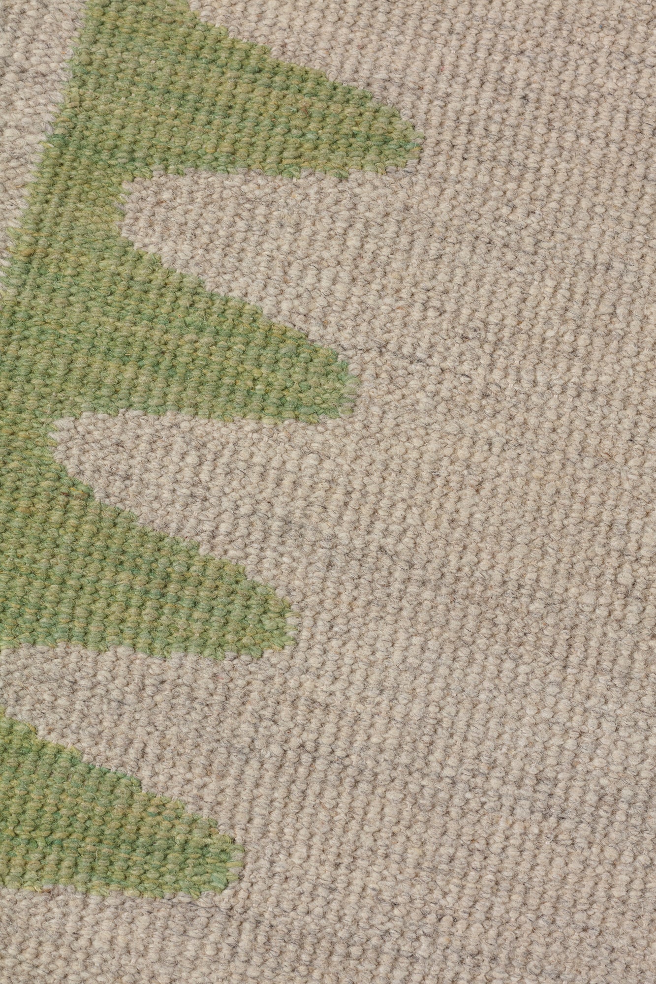Detail of the Waver Rug in Sage, a strated taupe field with a sage green flame stitch border. 