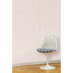 A white swivel chair in front of a wall papered in a large-scale repeating leaf print in white on a light pink watercolor background.