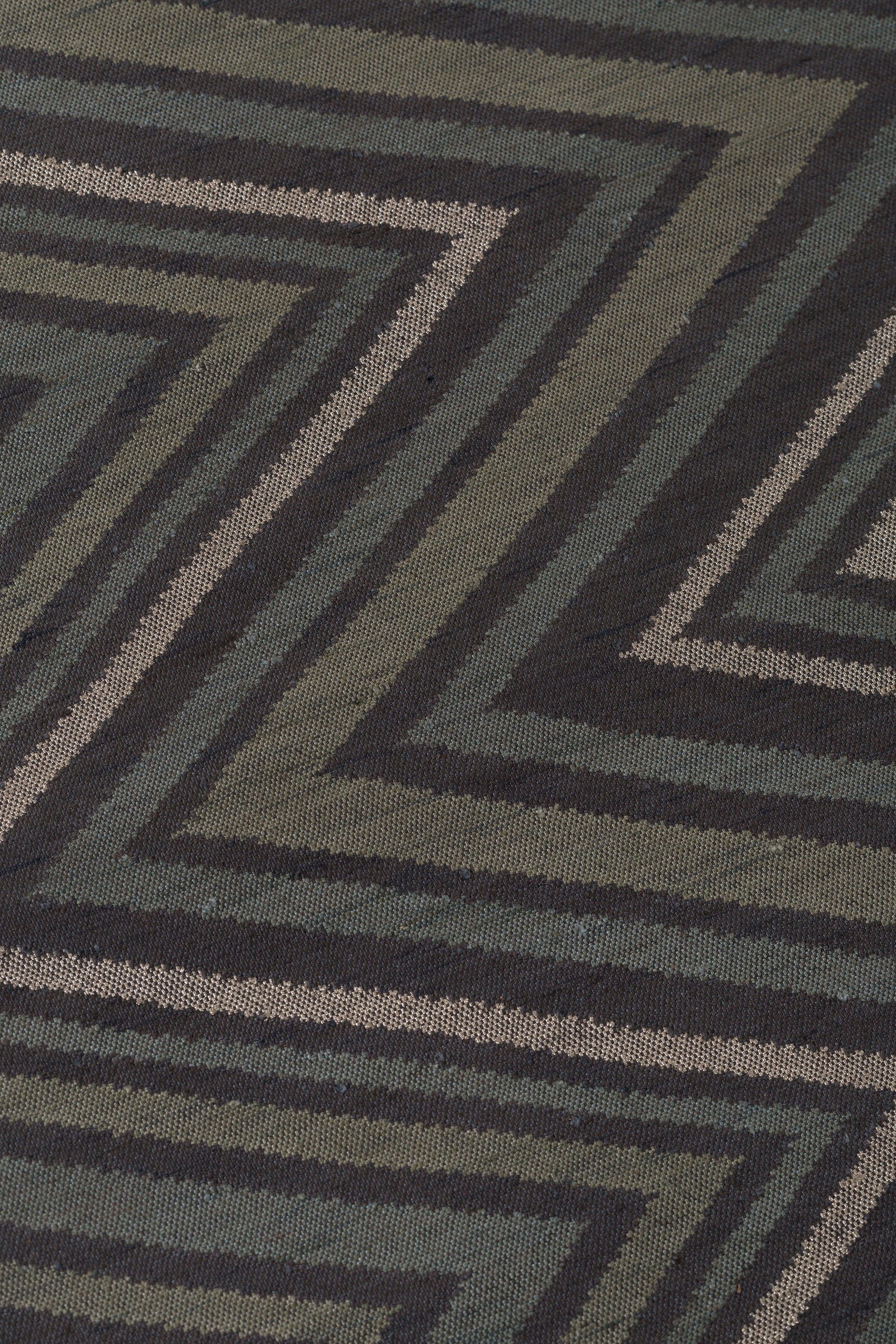 Detail of To The Point Rug in Pyrite-Metallic, a zig zag pattern in dark greens, metallic ecru and black.