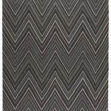 Full size To The Point Rug in Pyrite-Metallic, a zig zag pattern in dark greens, metallic ecru and black, with a mulit color tasseled edge. 