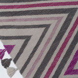 Detail of the Zig Zag Rug in Ruby-Rose, a mutli color zig zag pattern in fucshia, magenta, link and charcoal on a white field with a tassled edge. 
