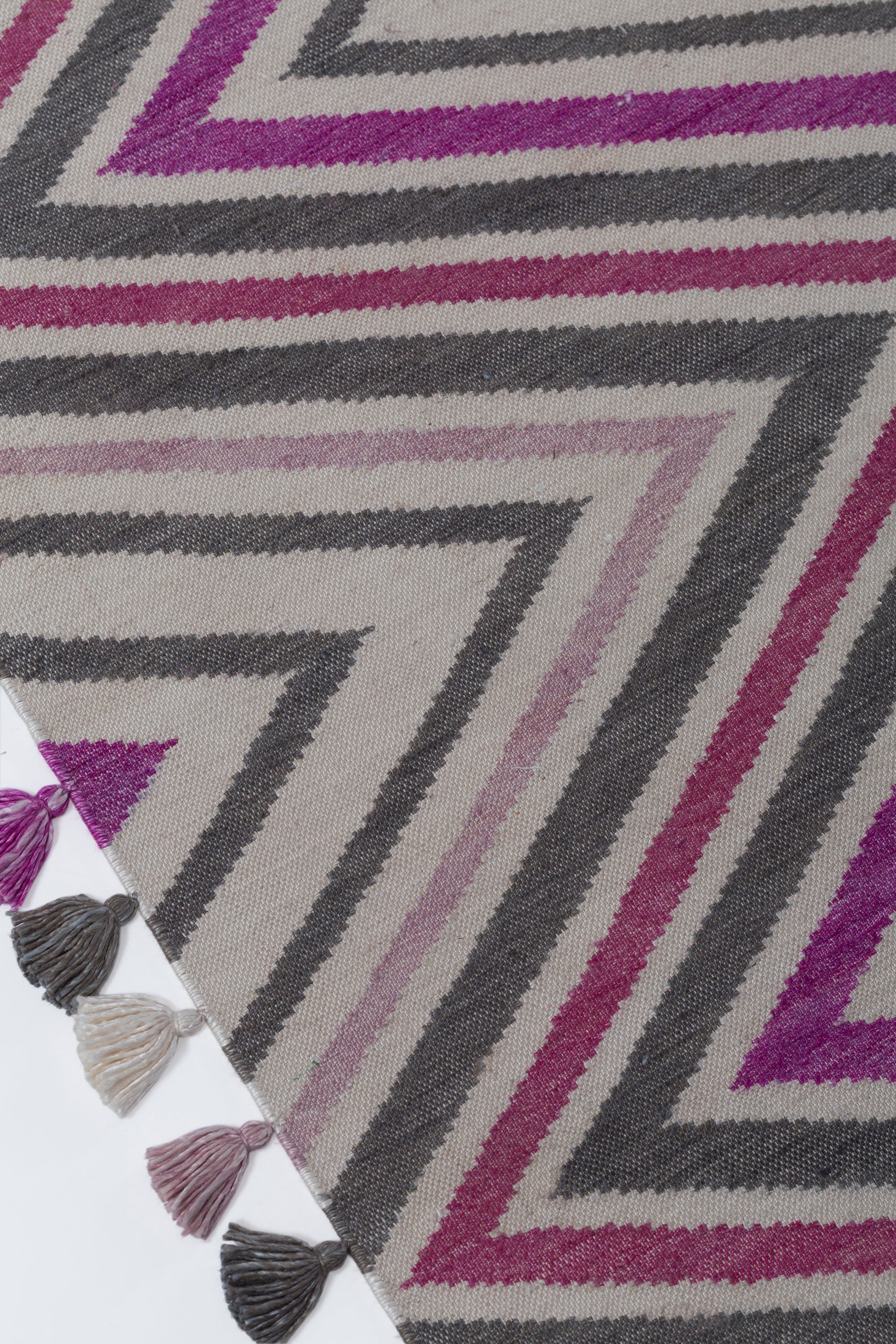 Detail of the Zig Zag Rug in Ruby-Rose, a mutli color zig zag pattern in fucshia, magenta, link and charcoal on a white field with a tassled edge. 