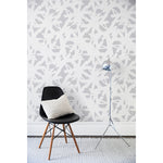 Chair and floor lamp in front of a wall papered in a bold white brushtroke pattern on a light gray background.