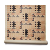 Partially unrolled wallpaper roll with layered geometric shapes in shades of black, beige and rust printed on a tan background.