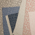 Pile of overlapping woven fabric swatches all in different colorways of the same large-scale repeating leaf print.